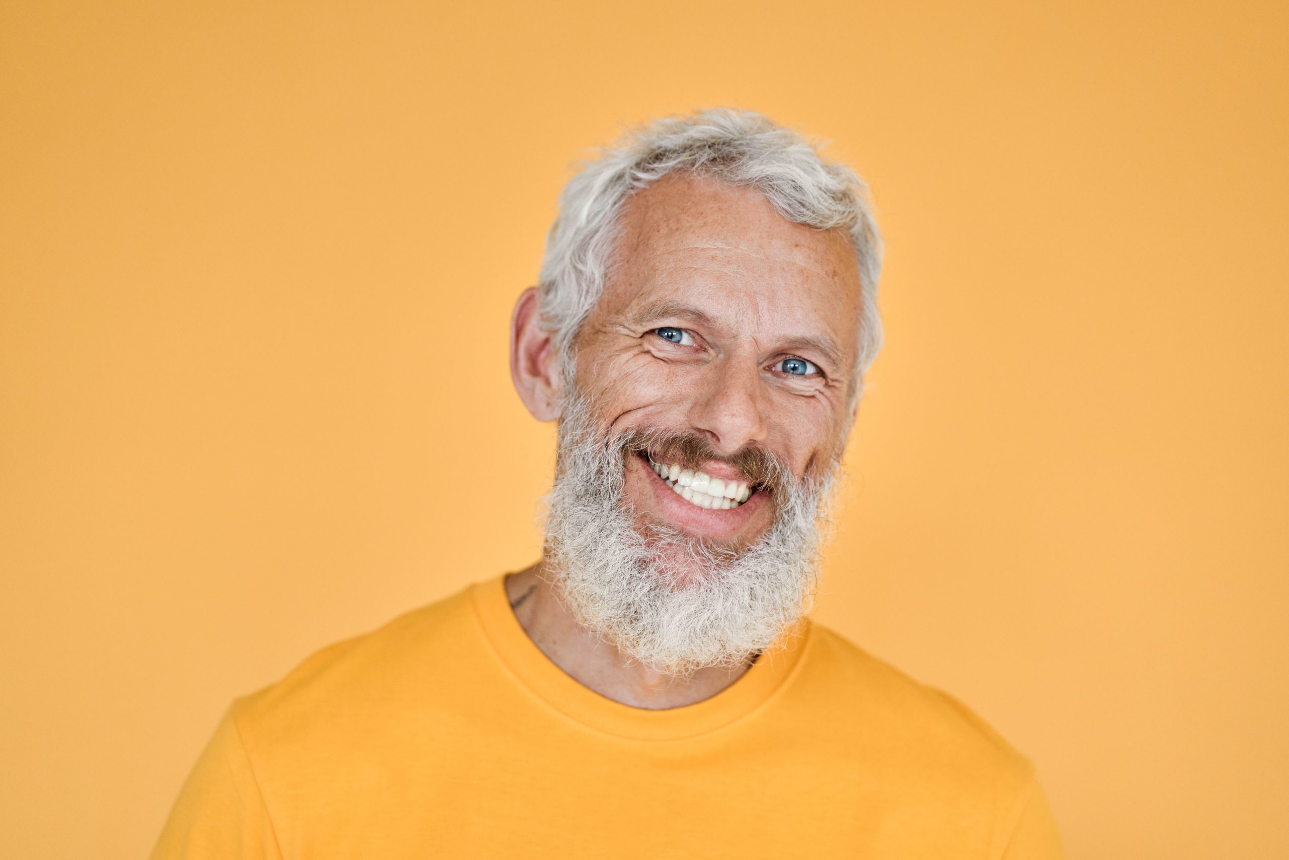 mature man who has completed dental implant therapy smiles at the camera on a yellow background