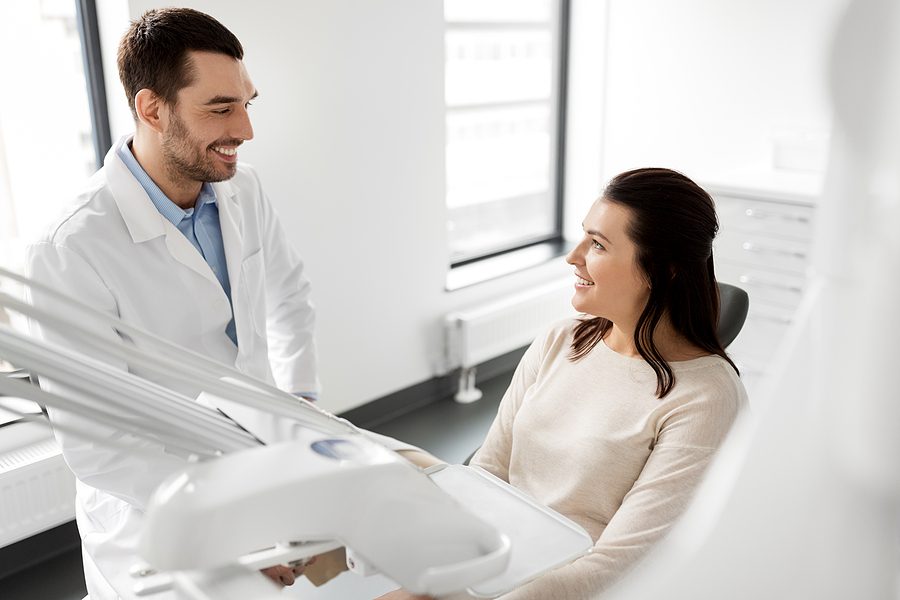 Woman sitting in dentist chair talking to male dentist in a white coat about a dental procedure. 
