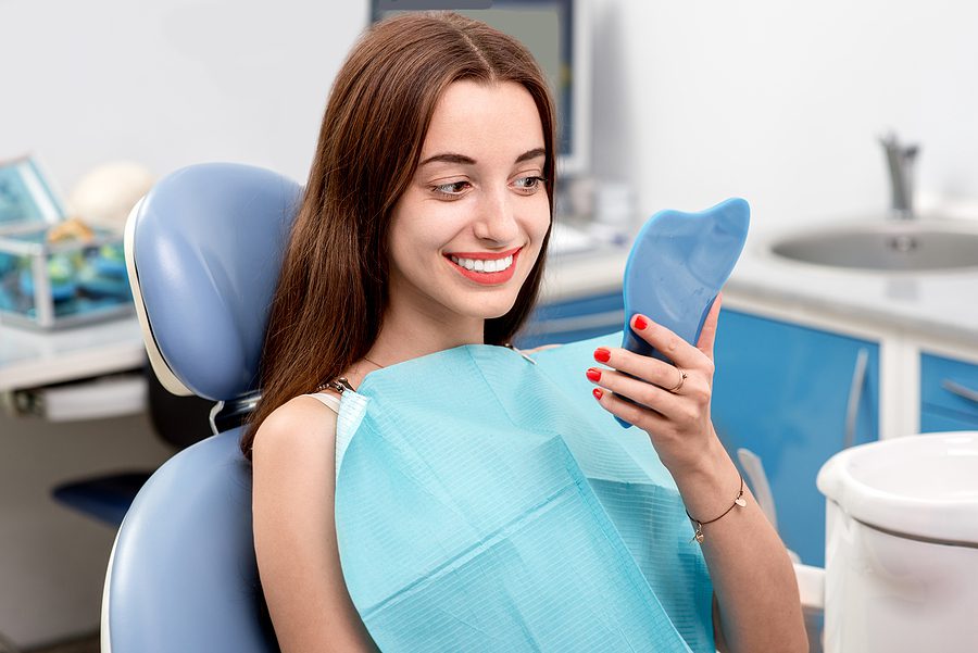 Young dental patient with long brown hair looking at her teeth in the mirror in the dental office. 