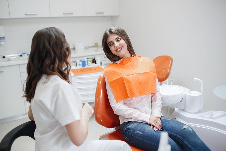 Female dental patient wearing a light colored shirt with an orange paper cover talking to the dentist after her procedure. 